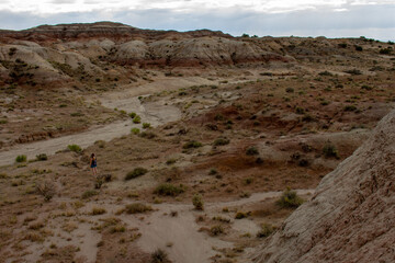 Distant female hiker walks along a dry river bed in the Bisti Badlands in the De-Na-Zin Wilderness in San Juan County, New Mexico