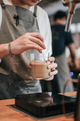 Fototapeta na wymiar Barista wear an apron stirring coffee while standing in a customer's order glass at bar counter.