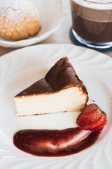Basque cheesecake with strawberry sauce on a table with hot chocolate and choux cream