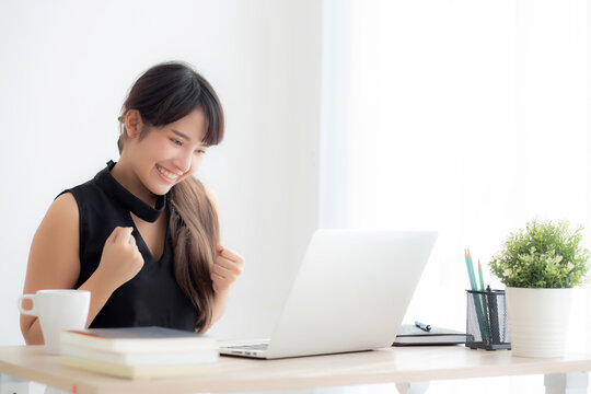 Beautiful portrait asian young woman smile working online laptop computer with happy satisfied sitting on desk office, girl using notebook with excited and glad, business and success concept.
