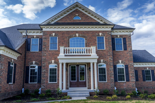 Classic American brick real estate house with Greek style triangle gabel decorative trim semi circle attic window, portico with fake balcony