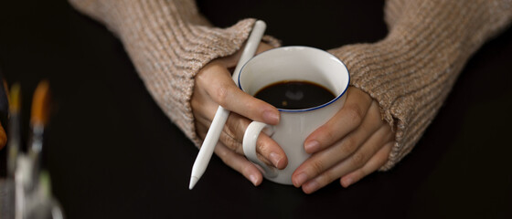 Female hands holding coffee cup and stylus pen while relaxing in office room