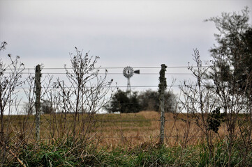 perimeter fence in a field with a diffuse windmill in the background	