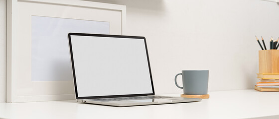 Modern study table with mock up laptop, coffee cup, mock up frame and stationery on white table