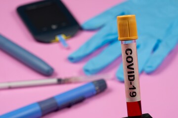 test tube with blood and writing covid-19 in the foreground, with blurred diabetes objects in the background