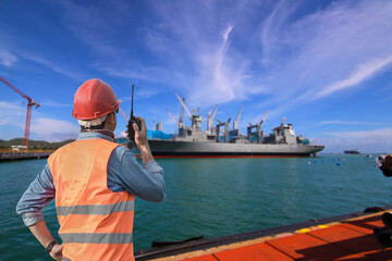 Worker with walkie talkie in shipyard on ship moored alongside in shipyard