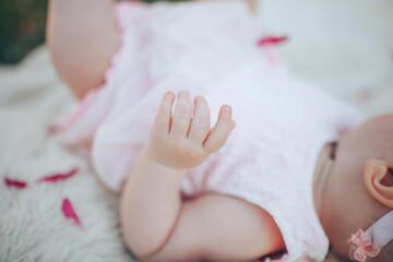 Fototapeta na wymiar Little newborn baby in a pink dress on a white plaid in a park