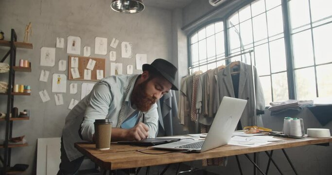 A male hipster clothing designer working in his office, redrawing his sketches to graphics tablet, making new collection - fashion concept 4k footage