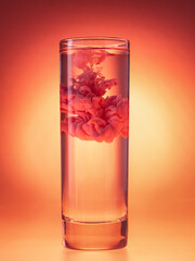 Red ink cloud in glass of water. Studio shot. Paint in water on red background. Monochrome color scheme