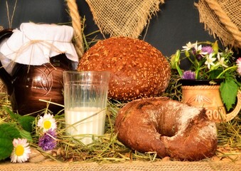 
Still life with black round rye bread and a glass of milk With a bouquet of flowers on a burlap background