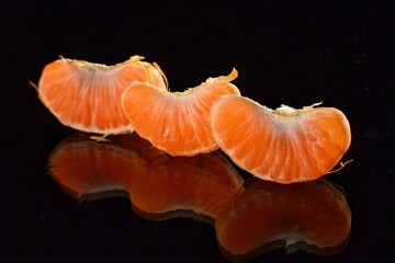 Peeled mandarin slices on a black mirror background