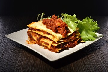 Meat lasagna on white square plates with lettuce leaf on black background