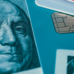 Part of a credit card and a hundred-dollar bill with a close-up portrait of Franklin on the entire image.