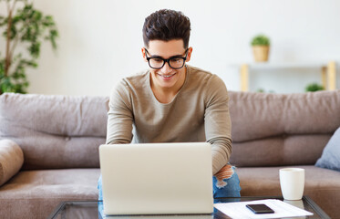 Friendly male freelancer using laptop on sofa.