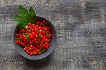red currant berries in a ceramic bowl on a rustic wooden background.