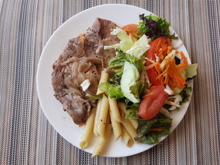 Steak with pasta and a salad with tomato and carrot