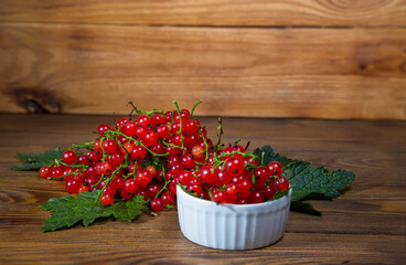 red currant berries in a ceramic bowl on a rustic wooden background.