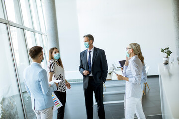 Business partners standing and looking at business results in office while wearing face masks sa an virus protection
