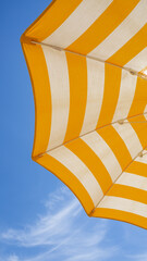 White and yellow striped beach umbrella. Blue sky in the background. View from below. Relaxing...
