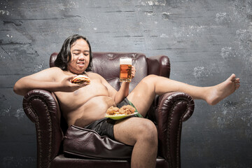 Asian fat man lying on the couch and eating fast food at home