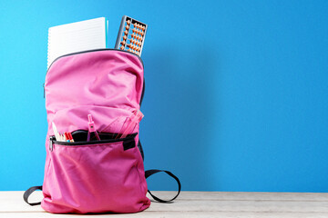 Backpack with book and stationary on wooden table with a blue background