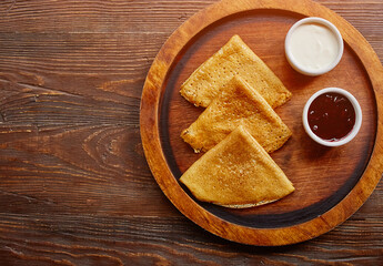 Homemade hot delicious pancakes with sour cream and jam on a wooden plate, top view.