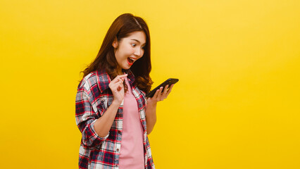 Portrait of surprised Asian female using mobile phone with positive expression, dressed in casual...