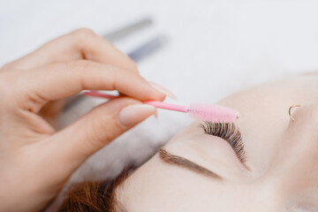 Eyelash extension procedure. Woman master combs lashes fake