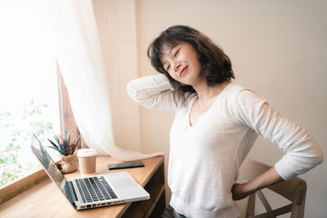 Young Asian worker woman taking short break while working from home. A tired woman having problem with office syndrome. A cup of coffee on table. Work from home concept