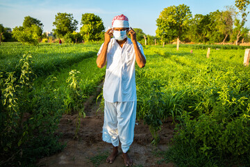 Indian farmer wearing mask standing in green field, agriculture, protection against covid-19 pandemic effect on people, new normal lifestyle.Zv