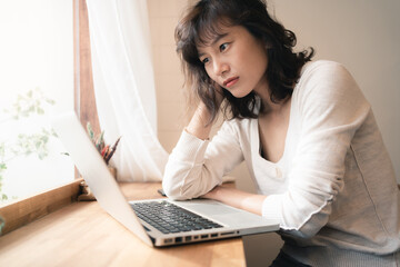 Young Asian worker woman working with laptop computer. A woman thinking of some idea and feeling stress while working from home. Social distancing concept