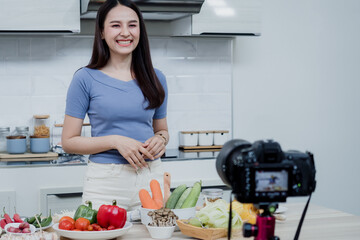 Social media concepts A happy woman standing in the kitchen using a camera and recording video online Happy Asian woman vlogger broadcast live online video Teaching to cook in the kitchen at home.