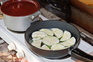 On the electric stove there is a pot with a lid and a frying pan with a dish of zucchini