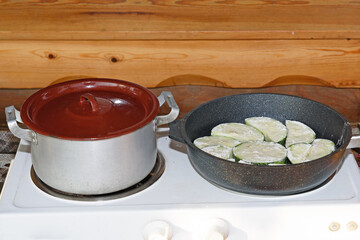 On the electric stove there is a pot with a lid and a frying pan with a dish of zucchini