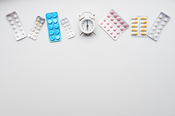 Different pills in blisters and alarm clock isolated on white background. 