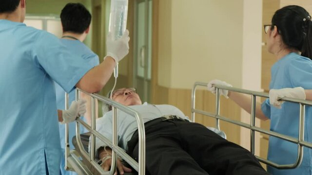Group of doctor, nurse and surgeon moving seriously injured patient lying on a stretcher through corridor in hospital. Medical staff in a hurry move emergency old patient into operating theater room.