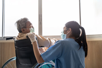 Asian nurse taking care of mature male patient sitting on wheelchair in hospital. Young woman and...