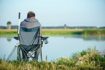 Fisherman sits on a chair by the lake and fishes.