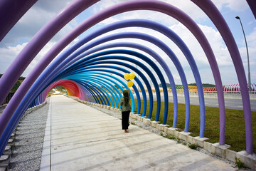 Woman carrying three yellow balloons below the rainbow poles architectures