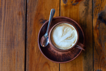 Coffee with milk in brown clay mug on wooden table. Top view