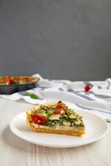 A Piece of Homemade Spinach Quiche on a white plate, side view.