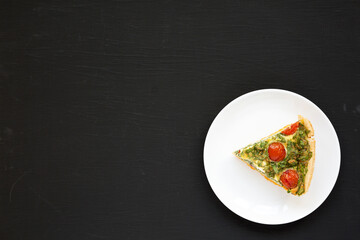 A Piece of Homemade Spinach Quiche on a white plate on a black surface, top view. Flat lay, overhead, from above. Copy space.