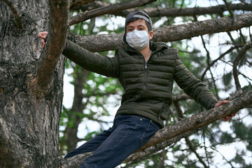 teenage boy poses on a tree, wearing a protective face mask - the concept of modern life and virus protection
