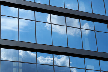 facade of a modern building on a bright Sunny day, blue sky and clouds reflecting in a glass,...