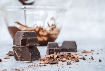 Pieces of dark chocolate with curls and chocolate cream on gray table.