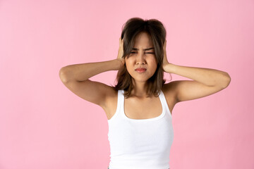 Frustrated young woman with eyes closed covering ears with hands against plain pink background