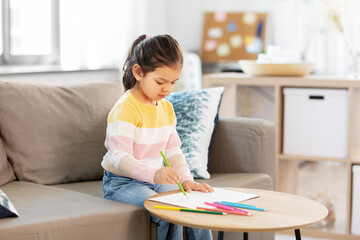 Naklejka premium childhood, creativity and art concept - little girl drawing with coloring pencils at home