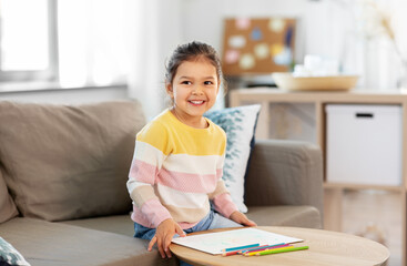 childhood, creativity and art concept - happy smiling little girl drawing with coloring pencils at home