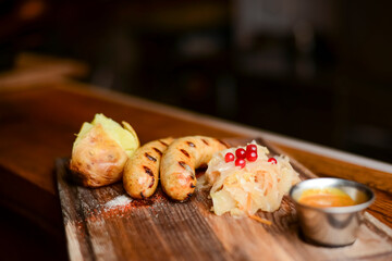 Baked potato with sausages and cabagge salad with sauce served on a wooden cutting board in a restaurant or cafe.