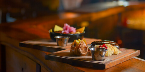 Baked potato with sausages and cabagge salad with sauce served on a wooden cutting board in a restaurant or cafe.